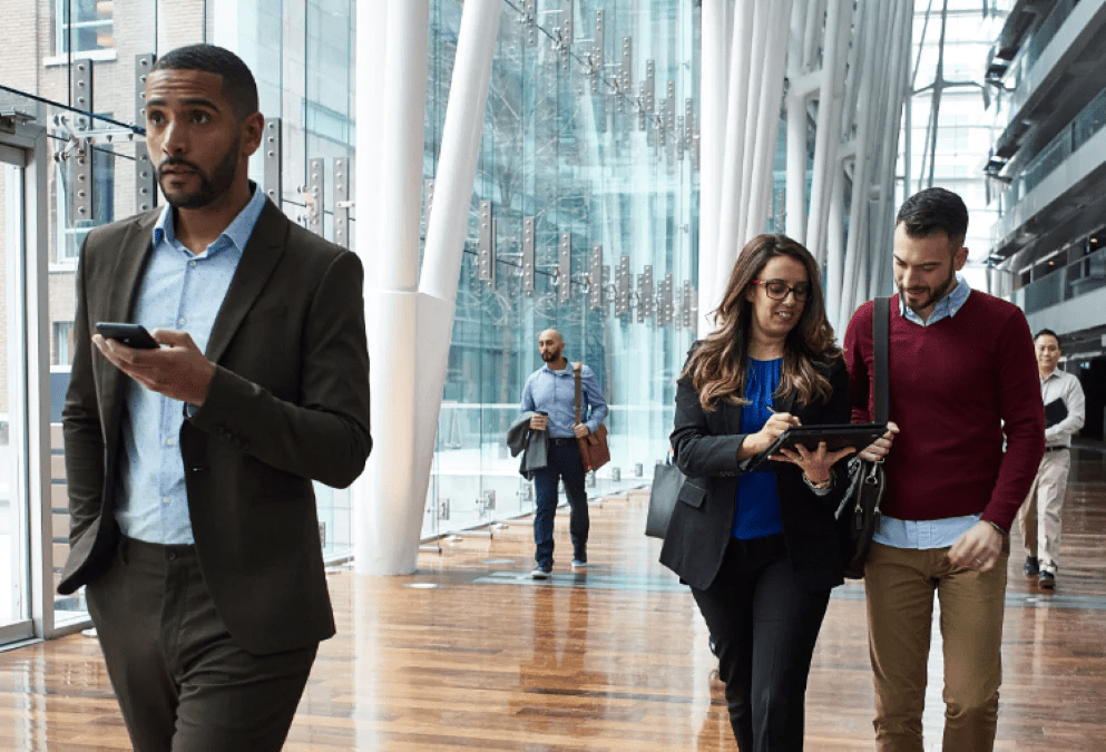 project-various-people-walking-through-a-large-glass-atrium-of-a-modern-building-one-is-holding-a-mobile-device-two-are-looking-at-a-tablet-device-interstellar-business-solutions-limited-ibsl