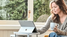 person-holding-a-coffee-cup-seated-at-a-small-table-using-a-surface-pro-6-interstellar-business-solutions-limited-ibsl