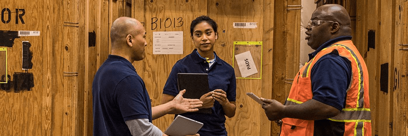 teams-three-people-using-tablet-devices-standing-and-talking-in-a-warehouse